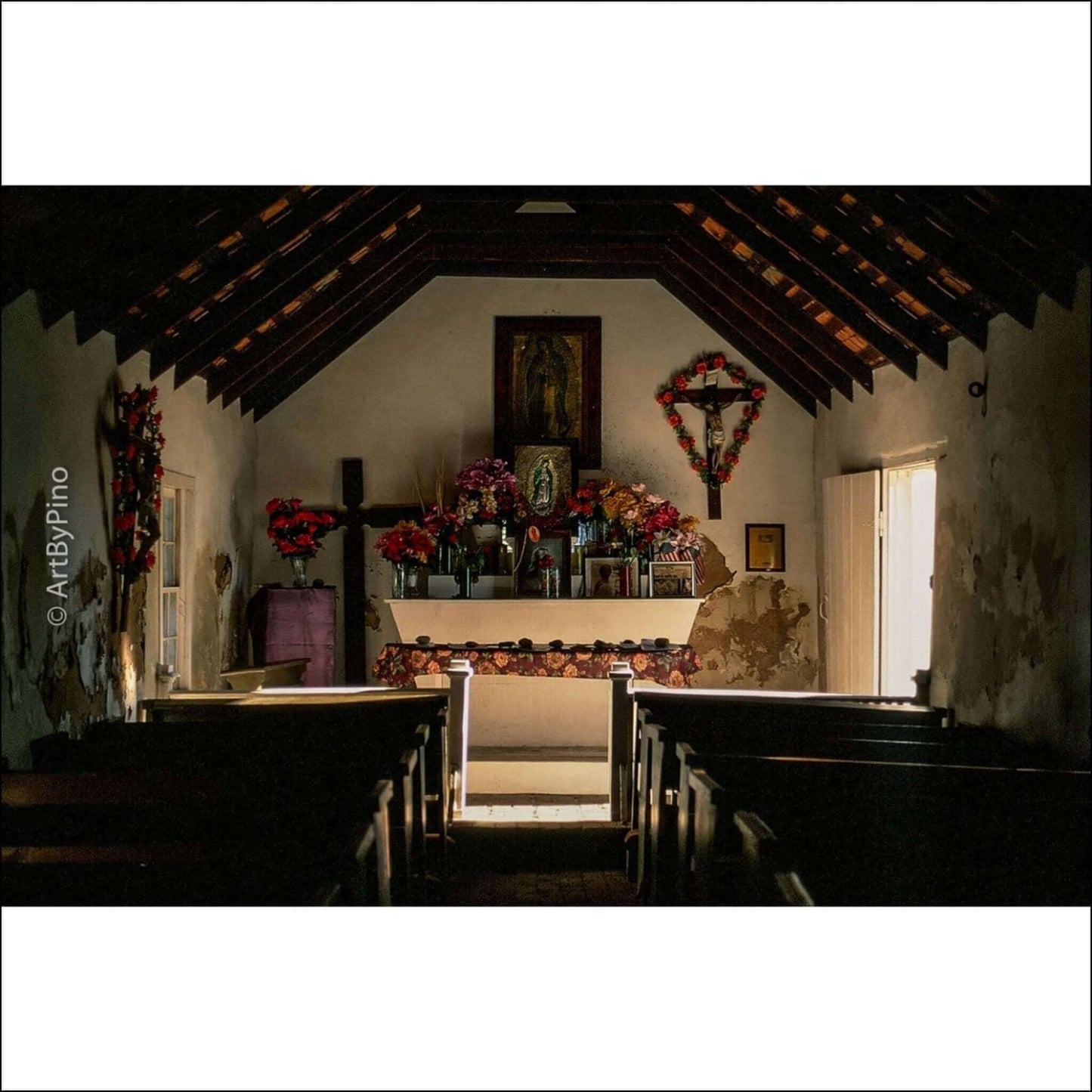 Interior view of a tranquil, rustic church with an altar adorned with flowers and a cross, illuminated by natural light.