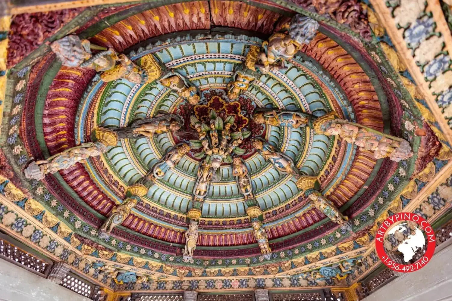 The ornate, multi-tiered ceiling features intricate carvings of figures and elaborate painted patterns in rich hues of gold, teal, maroon, and green.