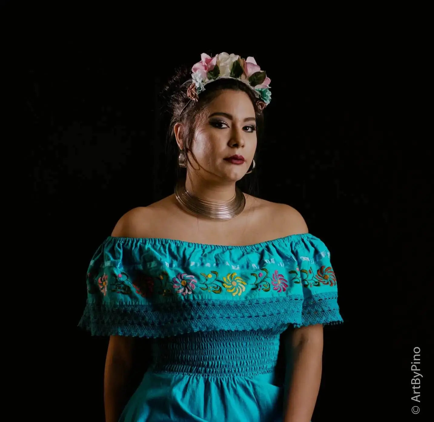 A woman wears a vibrant turquoise off-the-shoulder dress with intricate floral embroidery and lace trim.