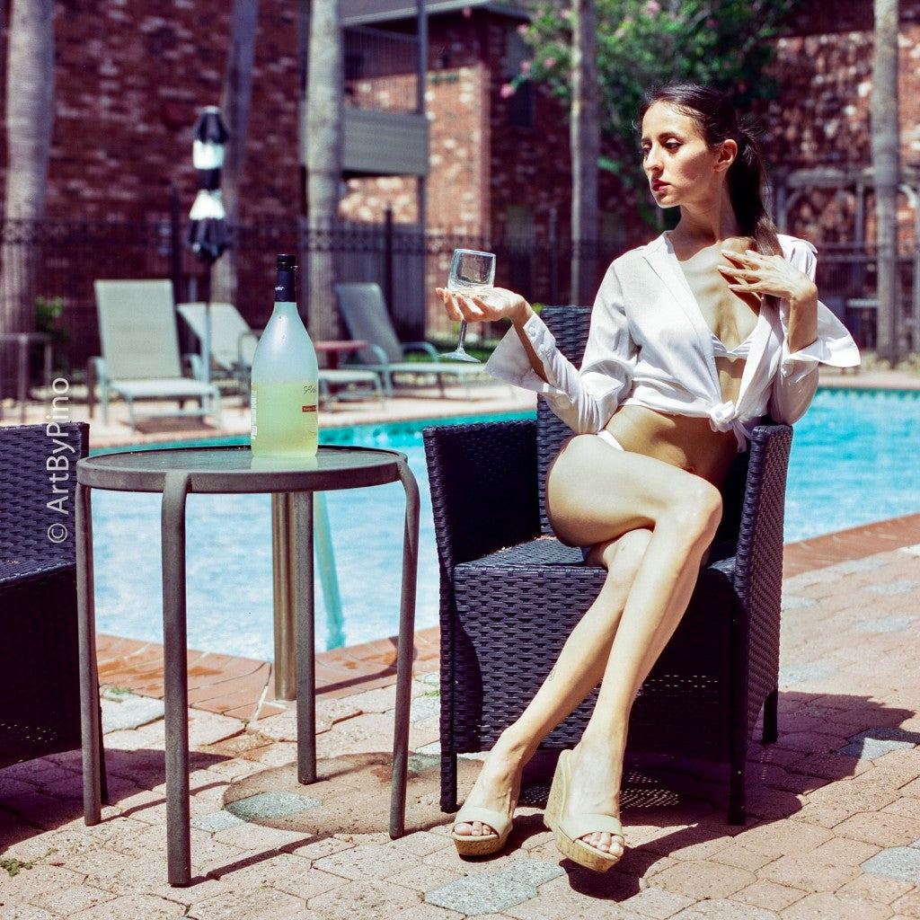 Woman in a white shirt over a bikini sitting poolside with a glass of white wine shot on CineStill 50D 120 film, developed in C-41