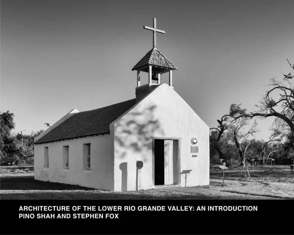 A small, white adobe church with a bell tower topped by a cross and a dark shingled roof.