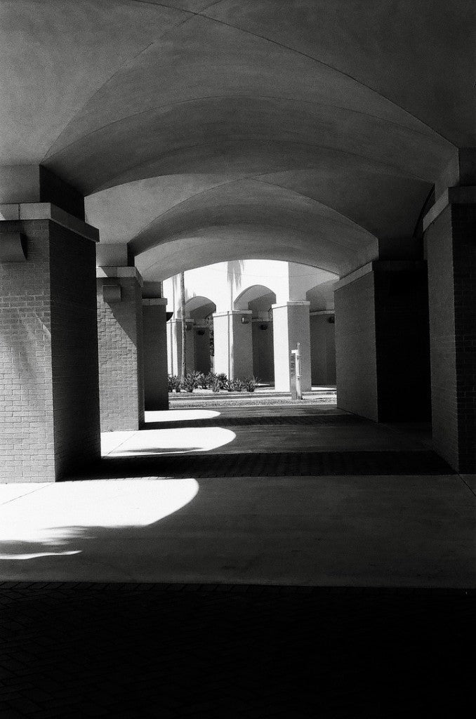 Vaulted arcade with brick pillars opening onto a sunlit courtyard — FOMA Fomapan 400 35mm, Pentax K1000