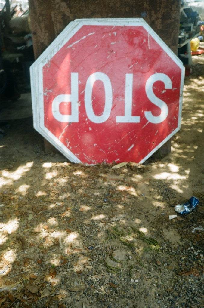 Weathered reversed STOP sign leaning against a pole on dirt and leaves, shot on Fujifilm 200 Japanese 35mm film, developed in Kodak C-41
