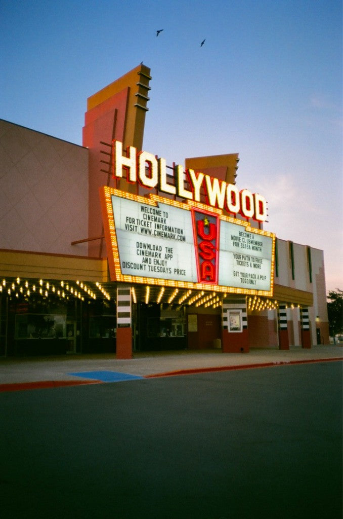 Dusk marquee of Cinemark Hollywood USA in McAllen, Texas, with HOLLYWOOD neon, USA sign, and birds overhead, shot on Fujifilm Supreme 400 35mm film, developed in Kodak C-41
