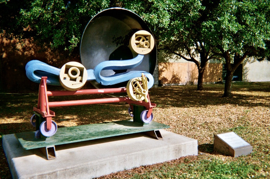 Colorful abstract steel sculpture with wheels and a large dish on a concrete base — Kodak FunSaver 800 disposable camera + 35mm