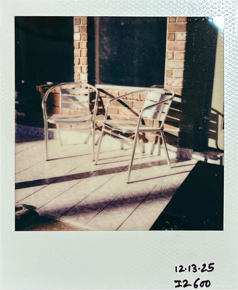 Polaroid I-2 + Polaroid 600 Color + Two silver metal café chairs on a sunlit tiled patio against a brick wall
