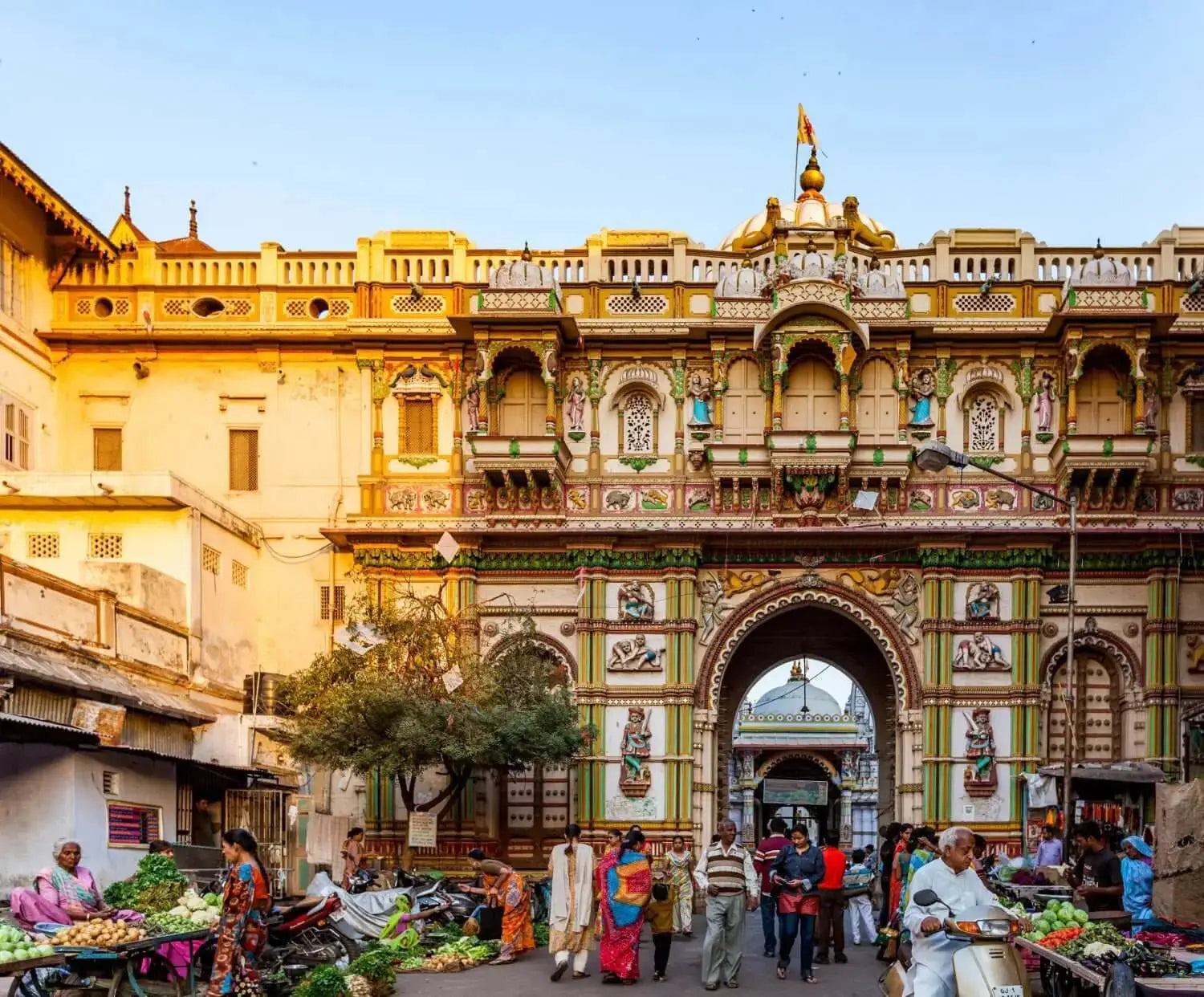The ornate, multi-tiered gateway of the historic palace complex features intricate carvings and vibrant gold, green, and cream-colored decorative elements.