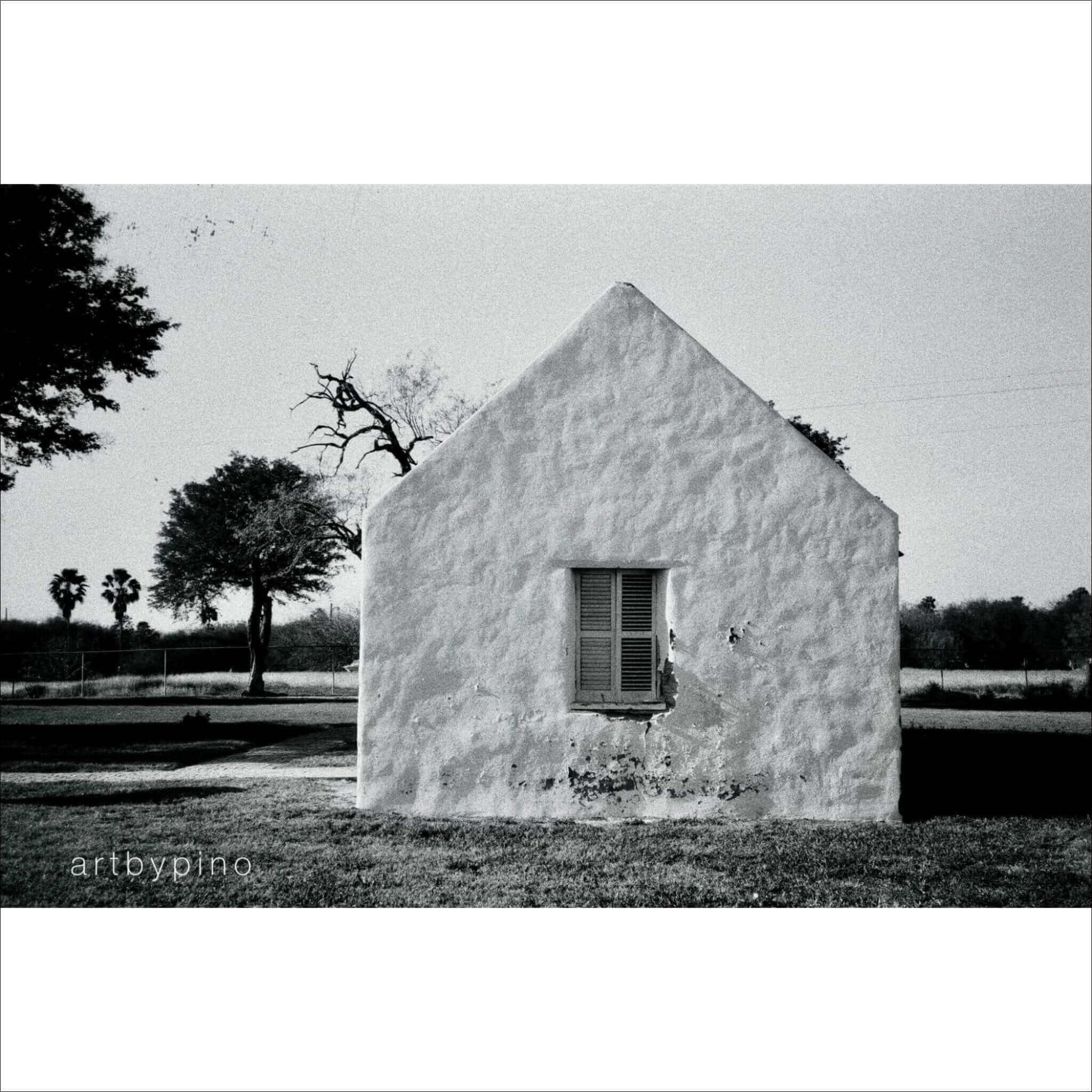 A white stucco house with a triangular roof and a single window featuring wooden shutters.