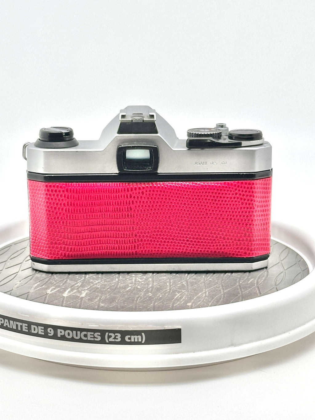 A vibrant pink camera with a textured, reptile-skin patterned body and silver metallic top plate.