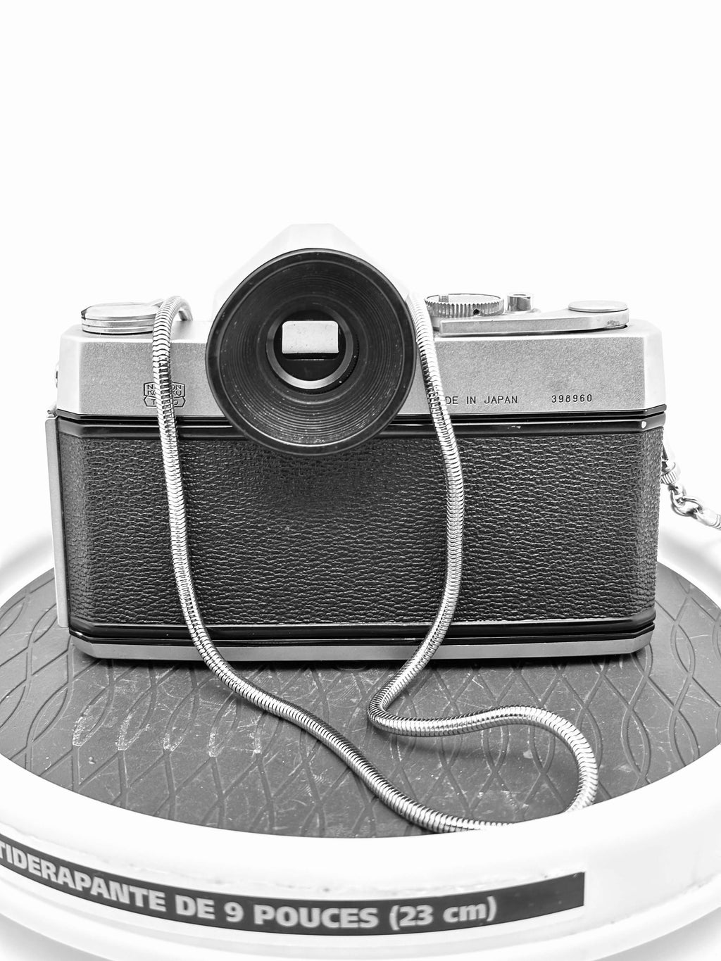 Silver and black vintage camera with textured leather body, chrome accents, and a coiled metal strap.
