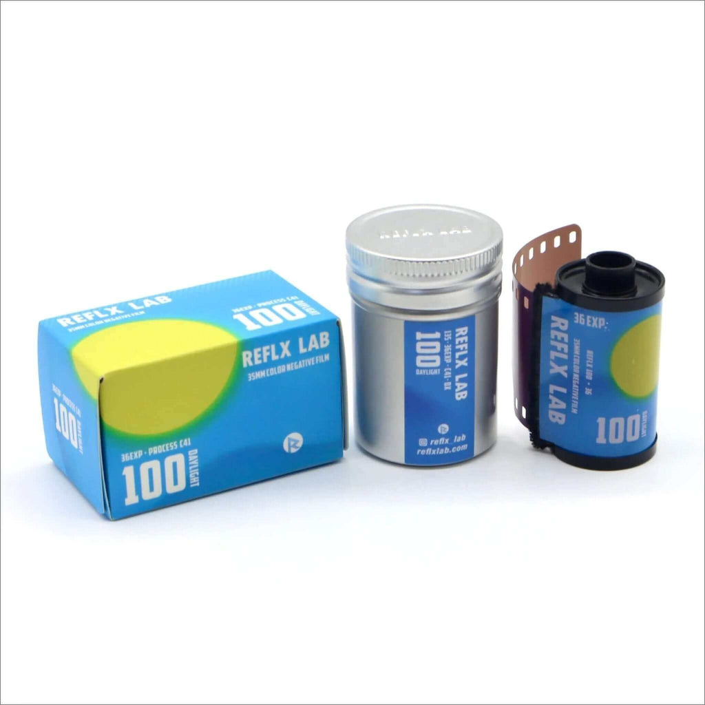 Blue and yellow reflex lab 100 iso 35mm color negative film box, silver canister with blue label, and a single roll of dark-colored film in its protective casing.