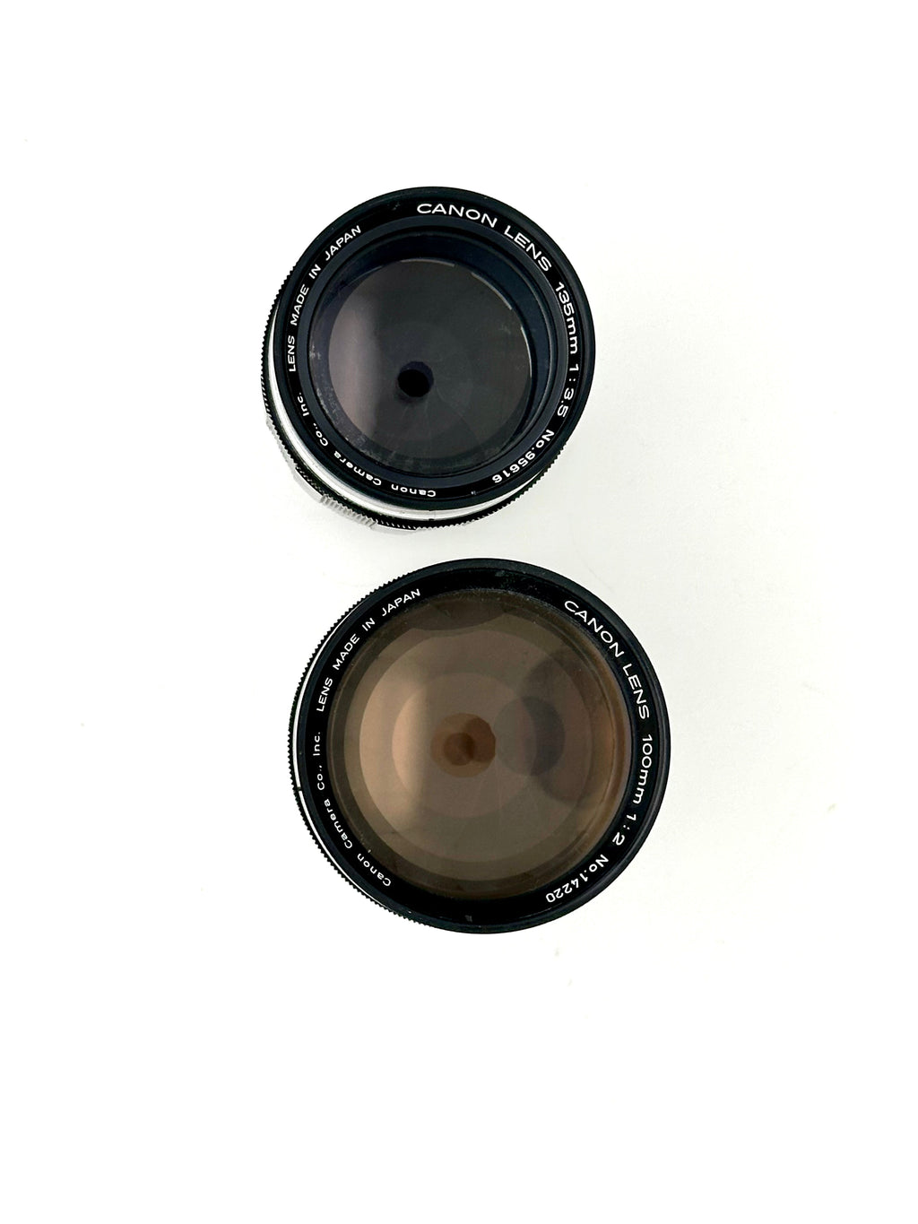 Two black canon camera lenses, one 50mm f/1.4 and the other 100mm f/2, with silver lettering on their rings.