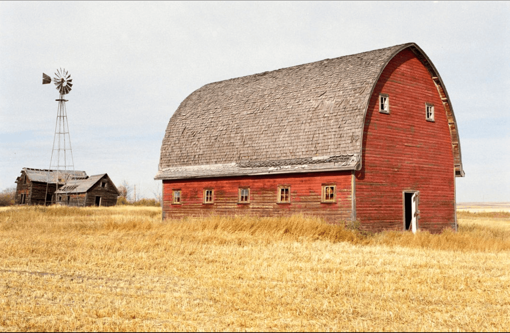 A weathered red wooden barn with a curved roof and gray shingles.