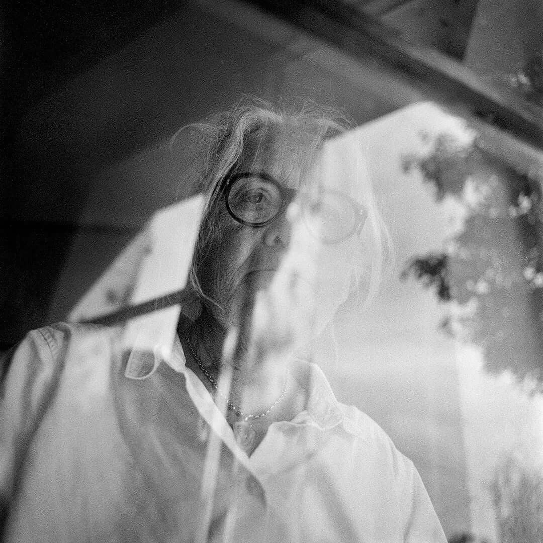 Black and white portrait of a person with glasses, captured through a reflective surface.