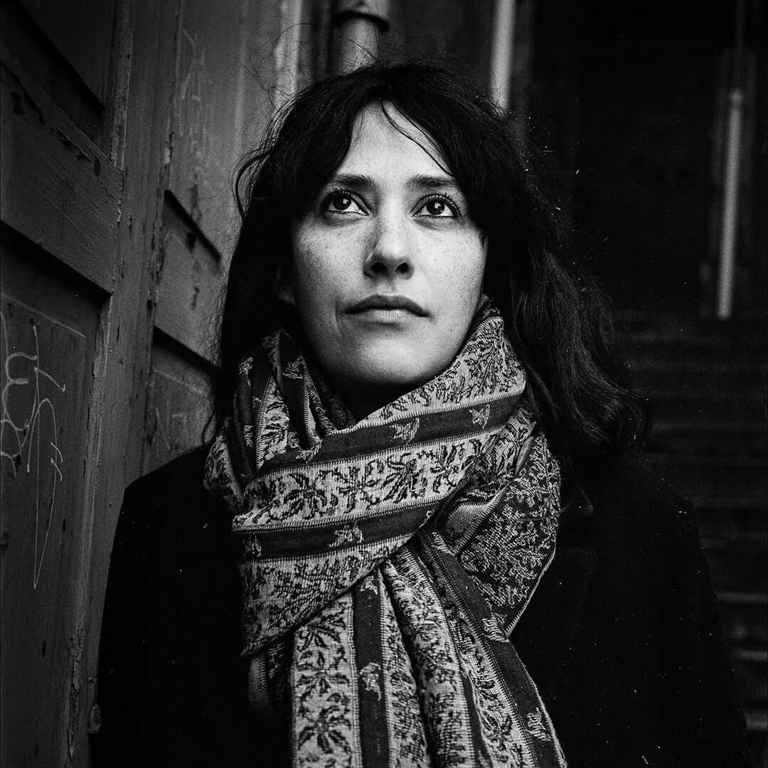 Woman in black and white portrait with patterned scarf, photographed in an urban setting.