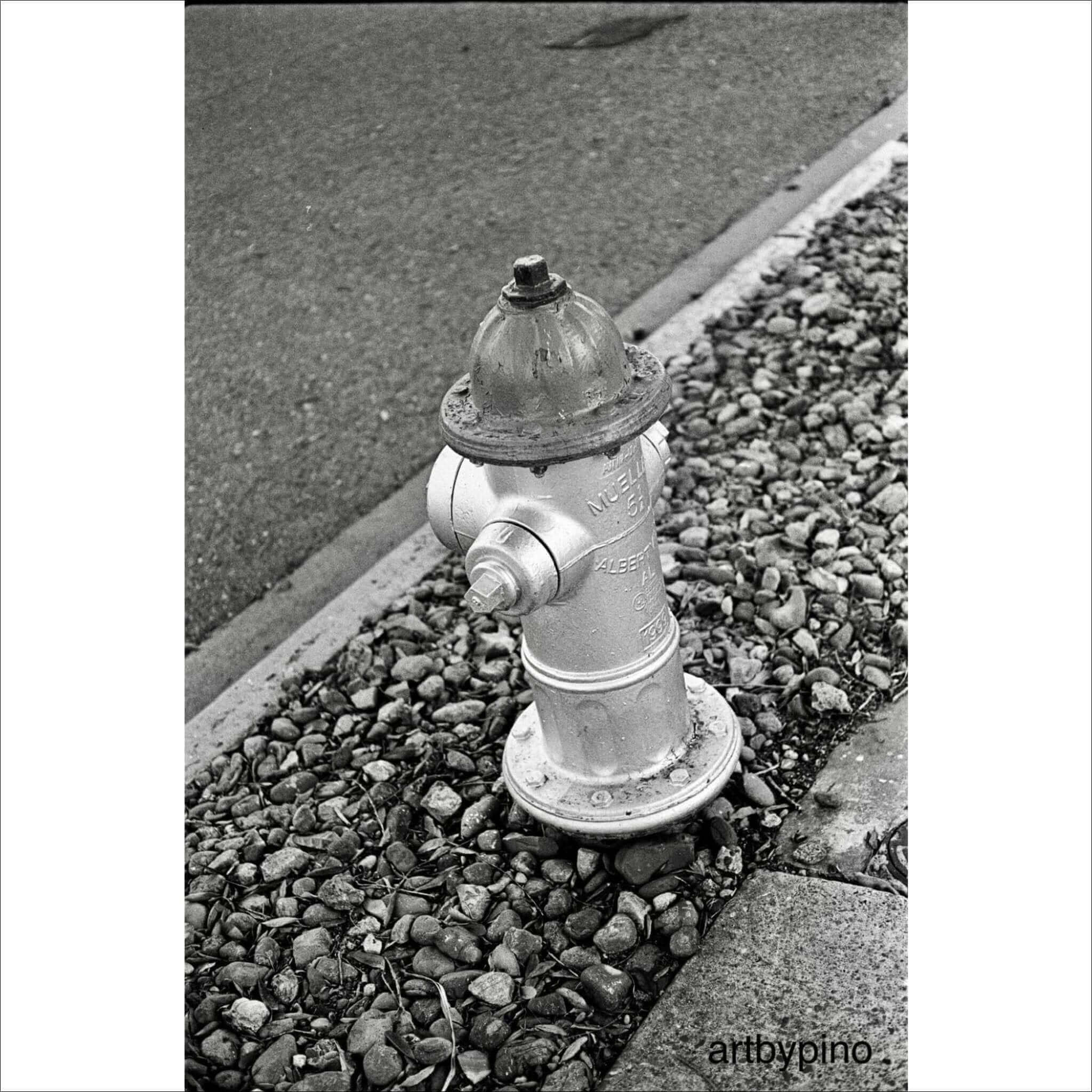 A classic silver fire hydrant with a domed top and bolted caps, standing on a bed of gravel.