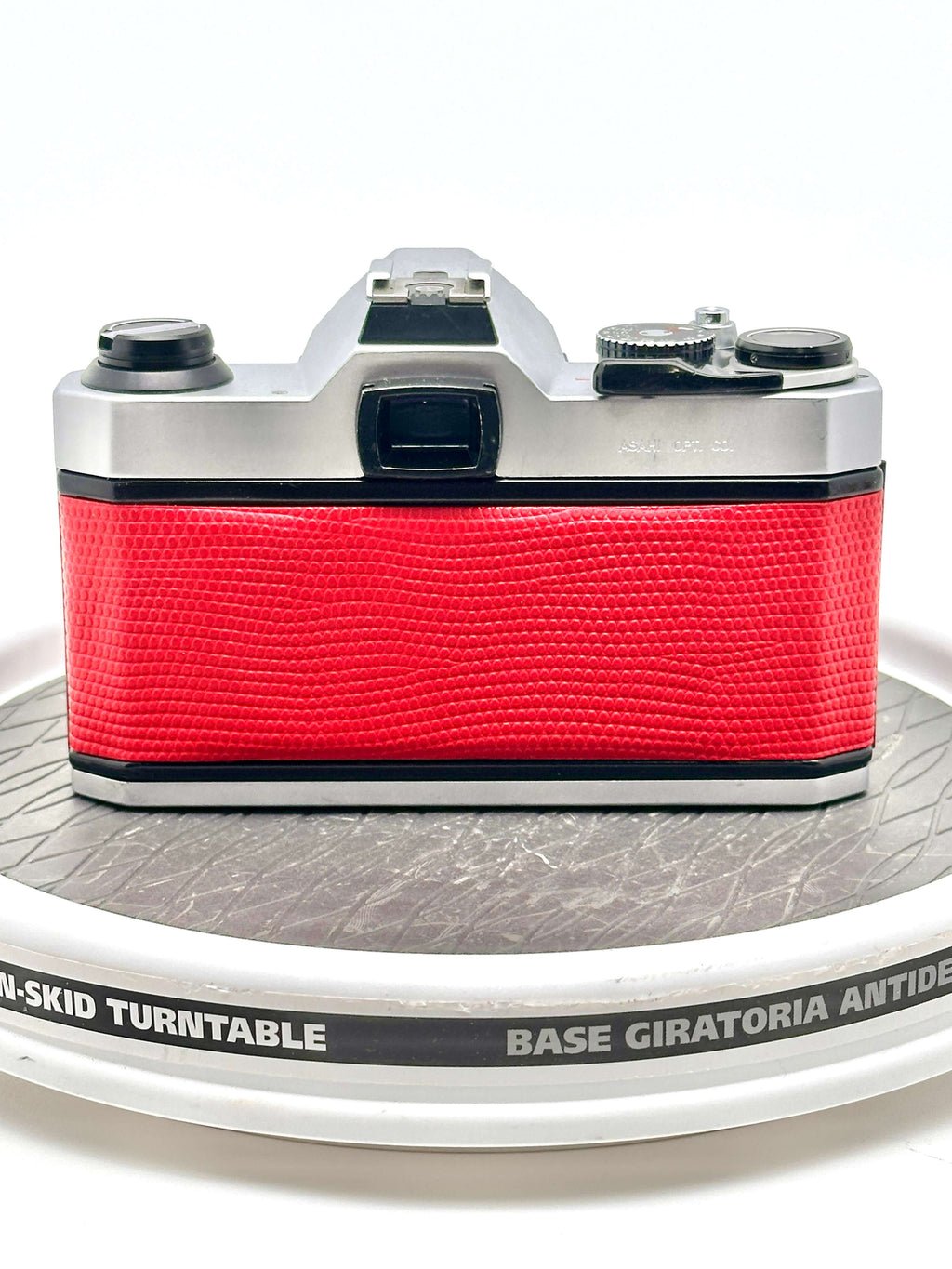 A vintage silver-bodied camera with a vibrant red textured leather grip.