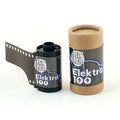 Black film canister with ’elektra 100’’ label and lightning bolt design, housed in a cylindrical cardboard tube.