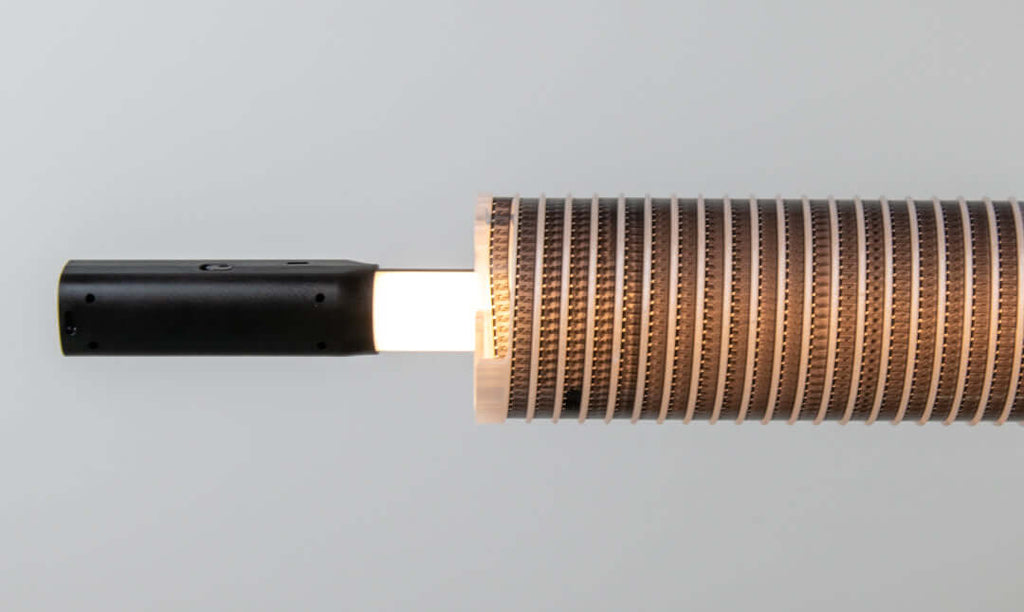 A sleek black cylindrical handle connects to a segmented, copper-toned heat exchanger with fine ridged grooves.