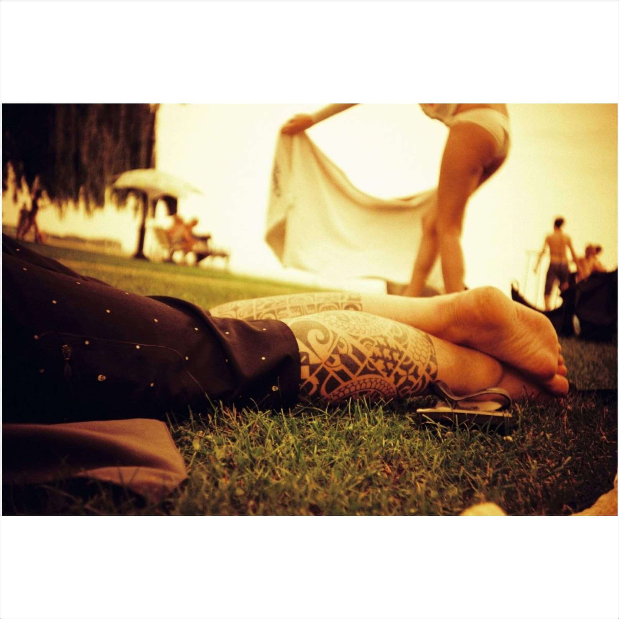 A person’s tattooed forearm and hand resting on grass, featuring intricate black tribal-style patterns.