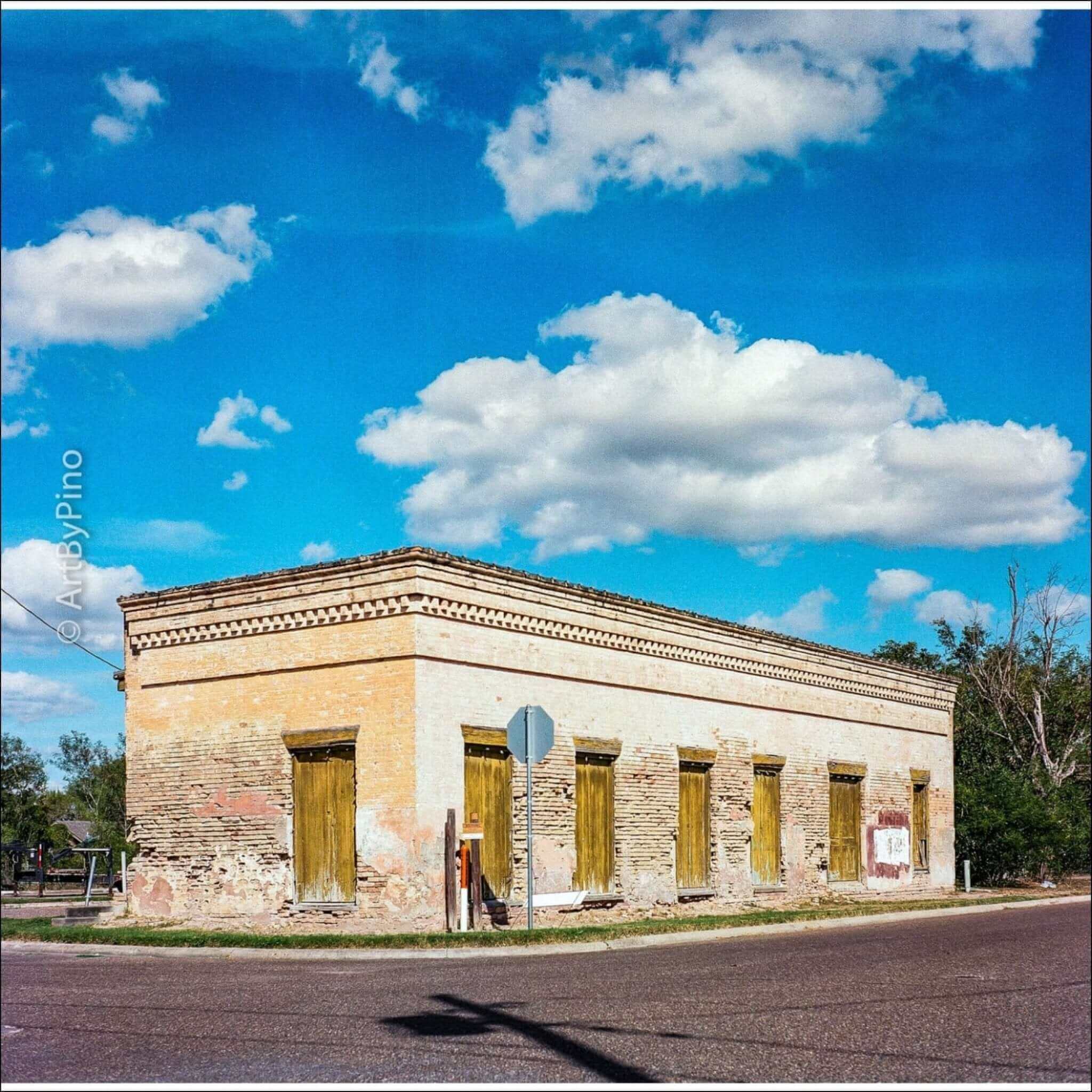 Weathered beige brick building with wooden shutters and a decorative cornice under a bright blue sky.