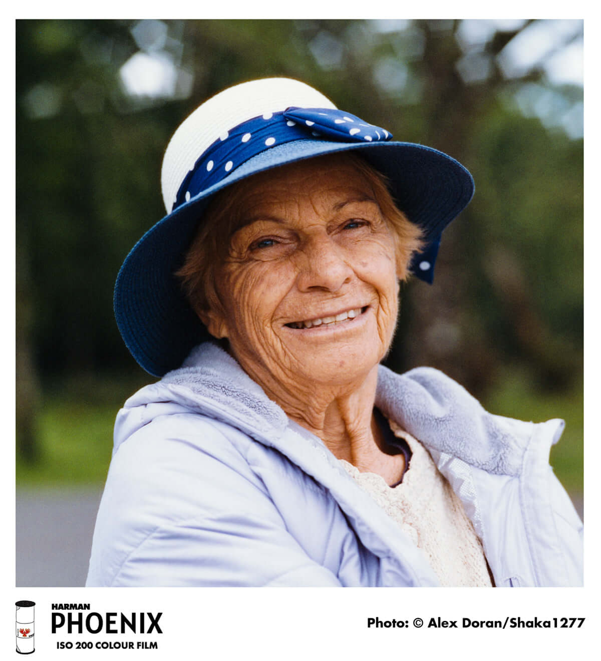 Elderly woman smiling outdoors, wearing a hat and a jacket, photographed with HARMAN Phoenix 200 ISO 120 Color Film