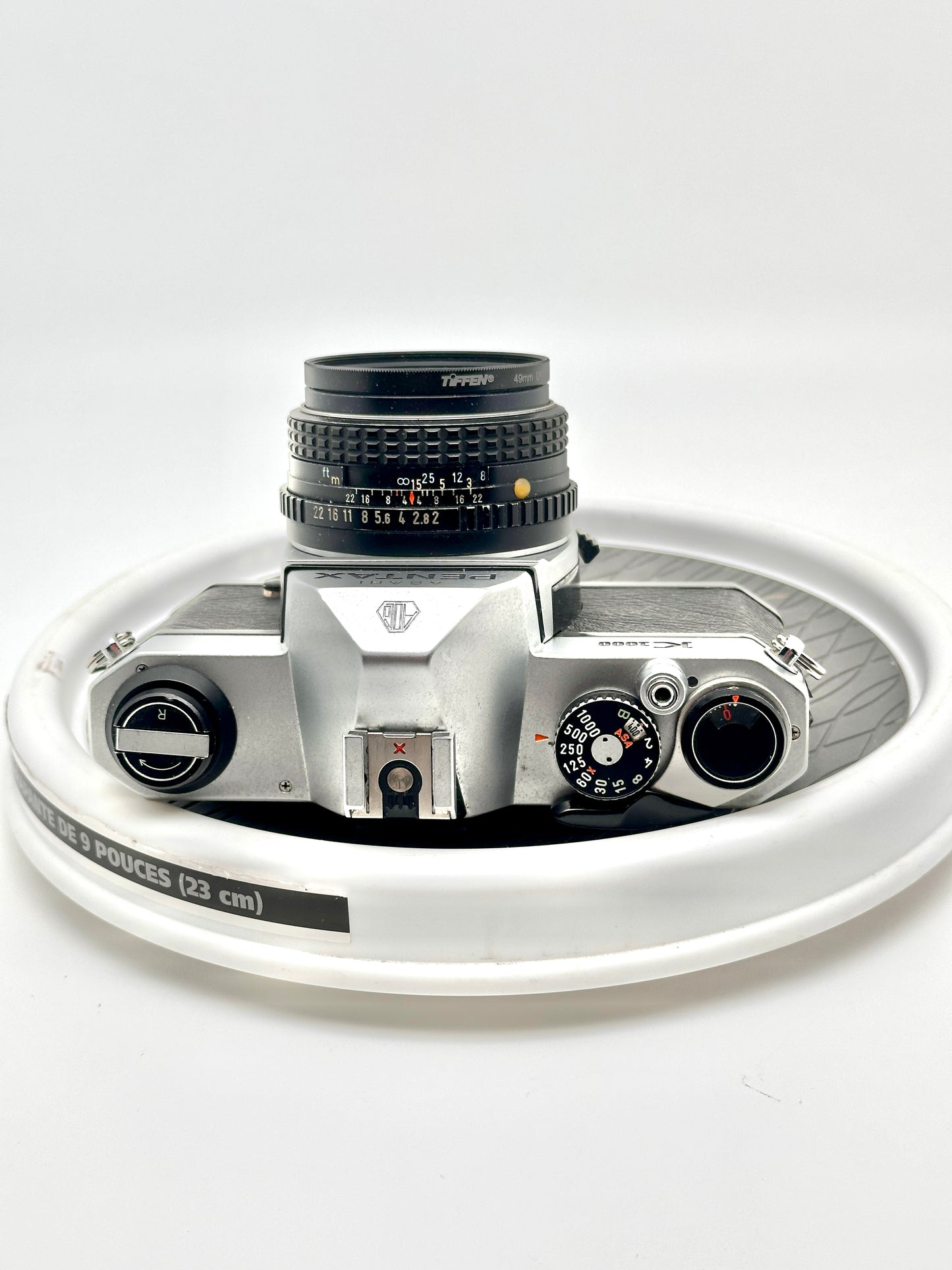 Top view of a used Pentax K1000 35mm film camera with a 50mm f2 lens on a white background.