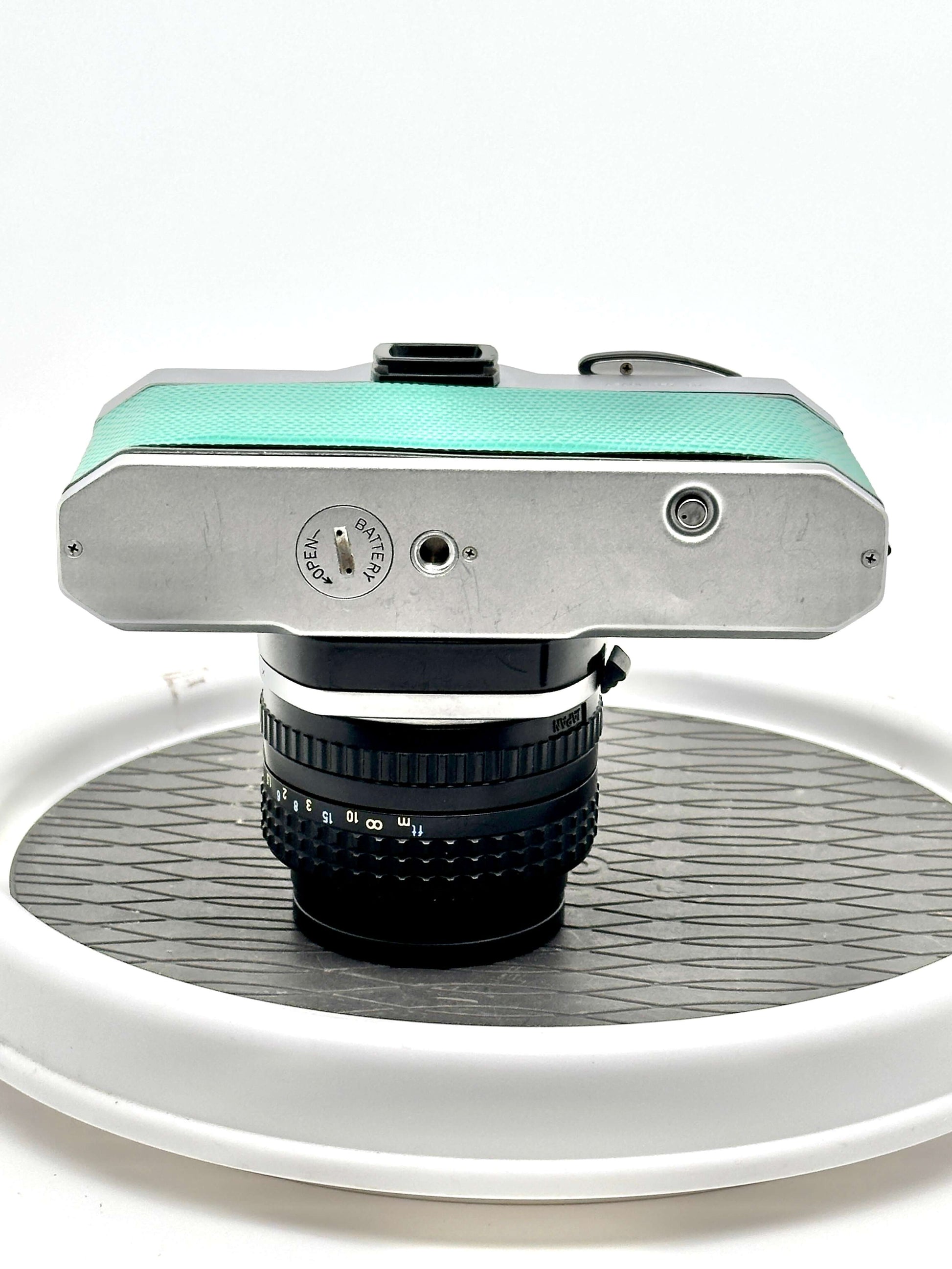 Top view of Japanese Asahi Pentax K1000 teal 35mm film camera with 50mm f1.4 lens on a display turntable.