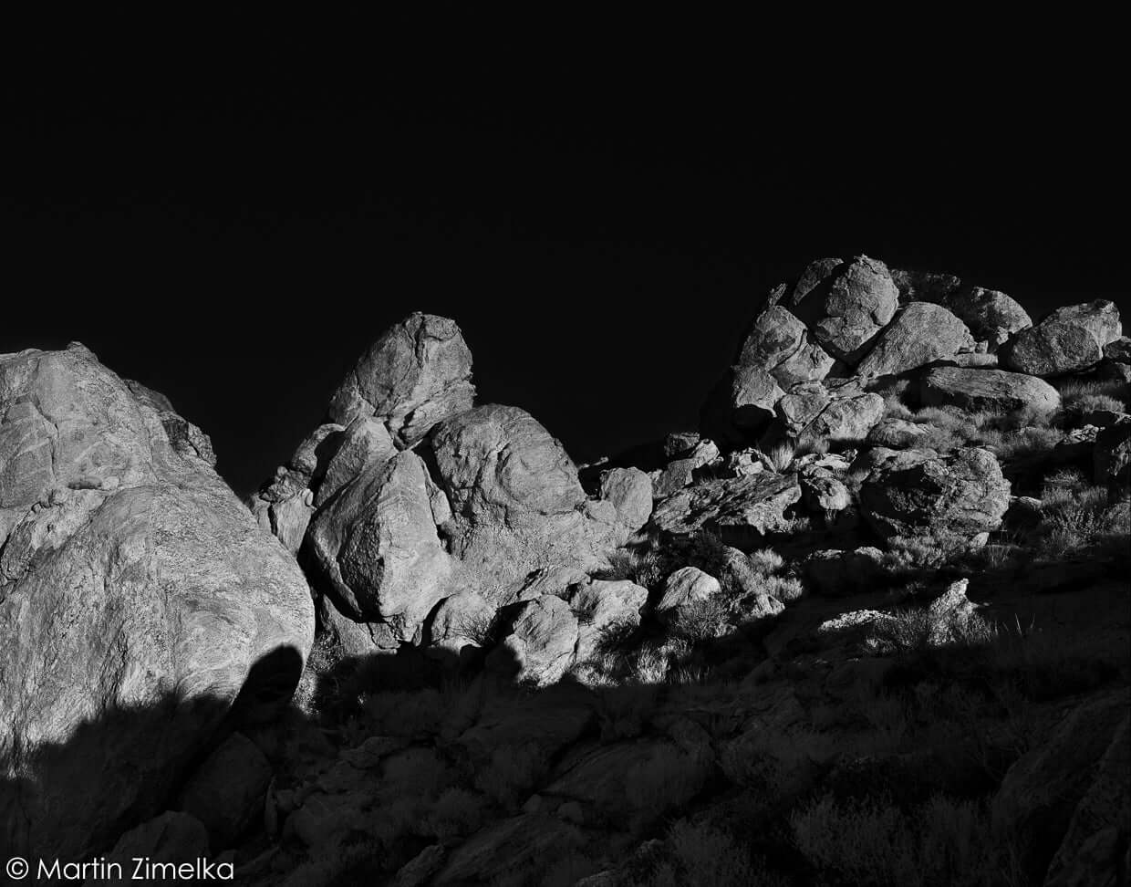 Black and white photograph of rugged rock formations under a dark sky by Martin Zimelka.