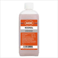 A translucent pink bottle of adox rodinal b/w film developer with a white cap and an orange label featuring black text.