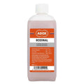 A translucent pink bottle of adox rodinal b/w film developer with a white cap and an orange label featuring black text.