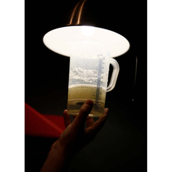 Hand holding a measuring beaker filled with liquid under a bright lamp.