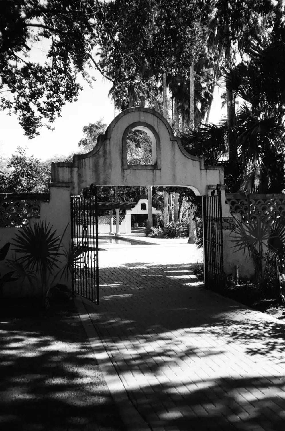 Arched stone gateway with wrought iron gates amid tropical foliage, shot on Catlabs x film Kodak Tri-x 400
