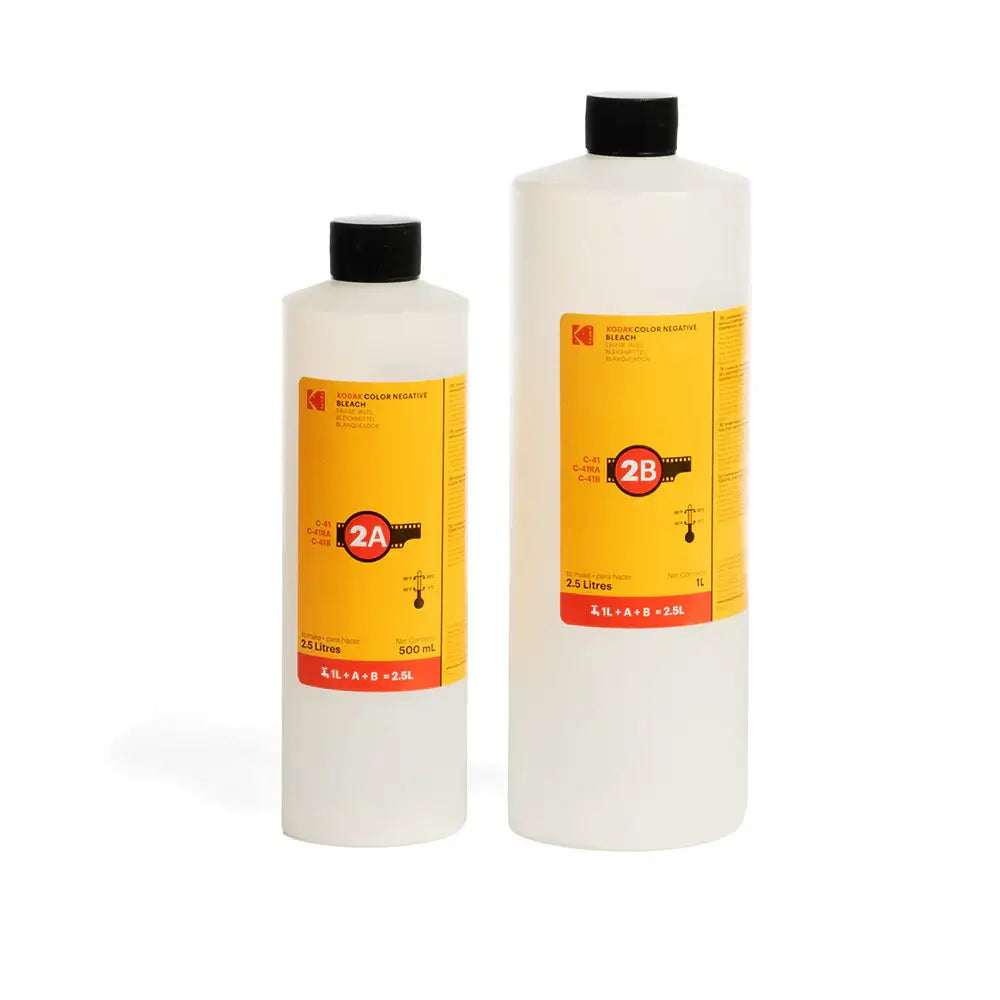 Two translucent plastic bottles of kodak color negative developer, one 500 ml and the other 2.5 litres, both with black caps and bright yellow labels featuring red accents and film strip graphics.
