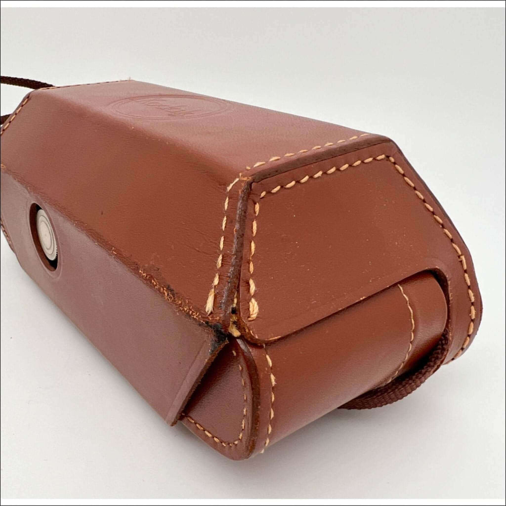 Brown leather camera case with tan stitching and a circular metal clasp.