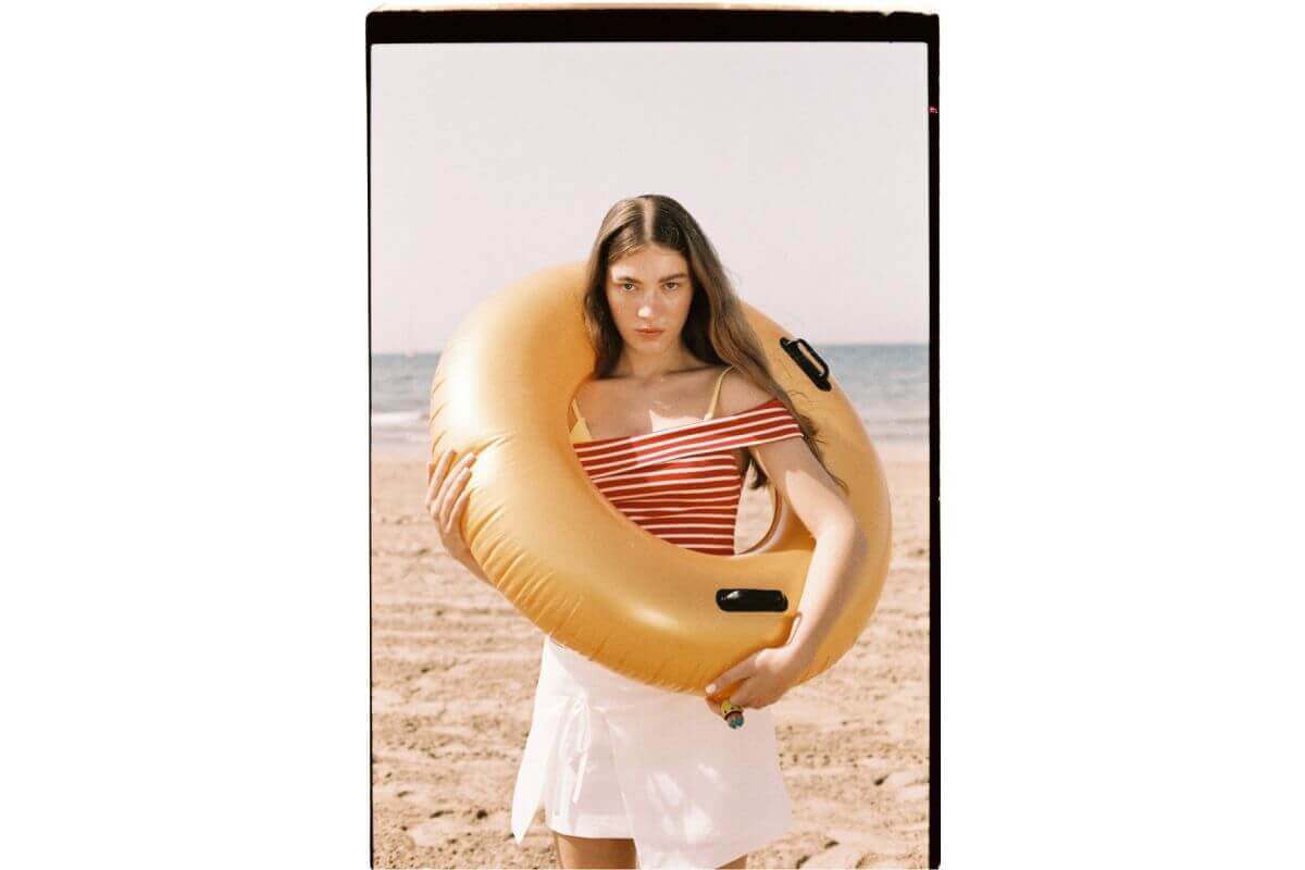 Young woman in a red striped top holding a golden inflatable ring on a beach.