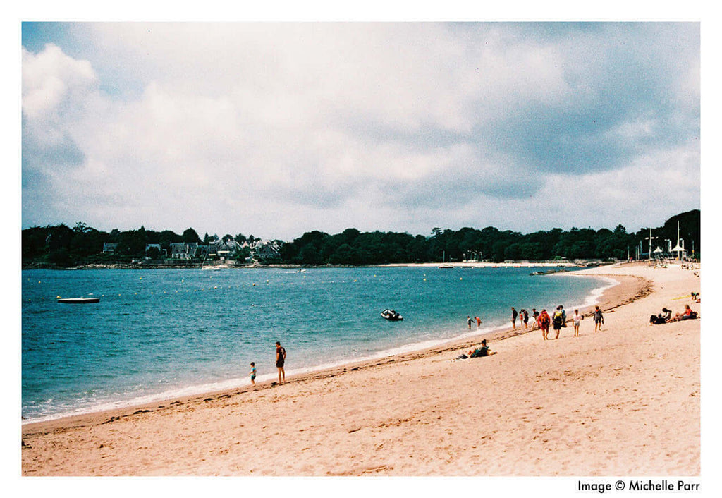 A scenic beach view with people enjoying the water and sand under cloudy skies.