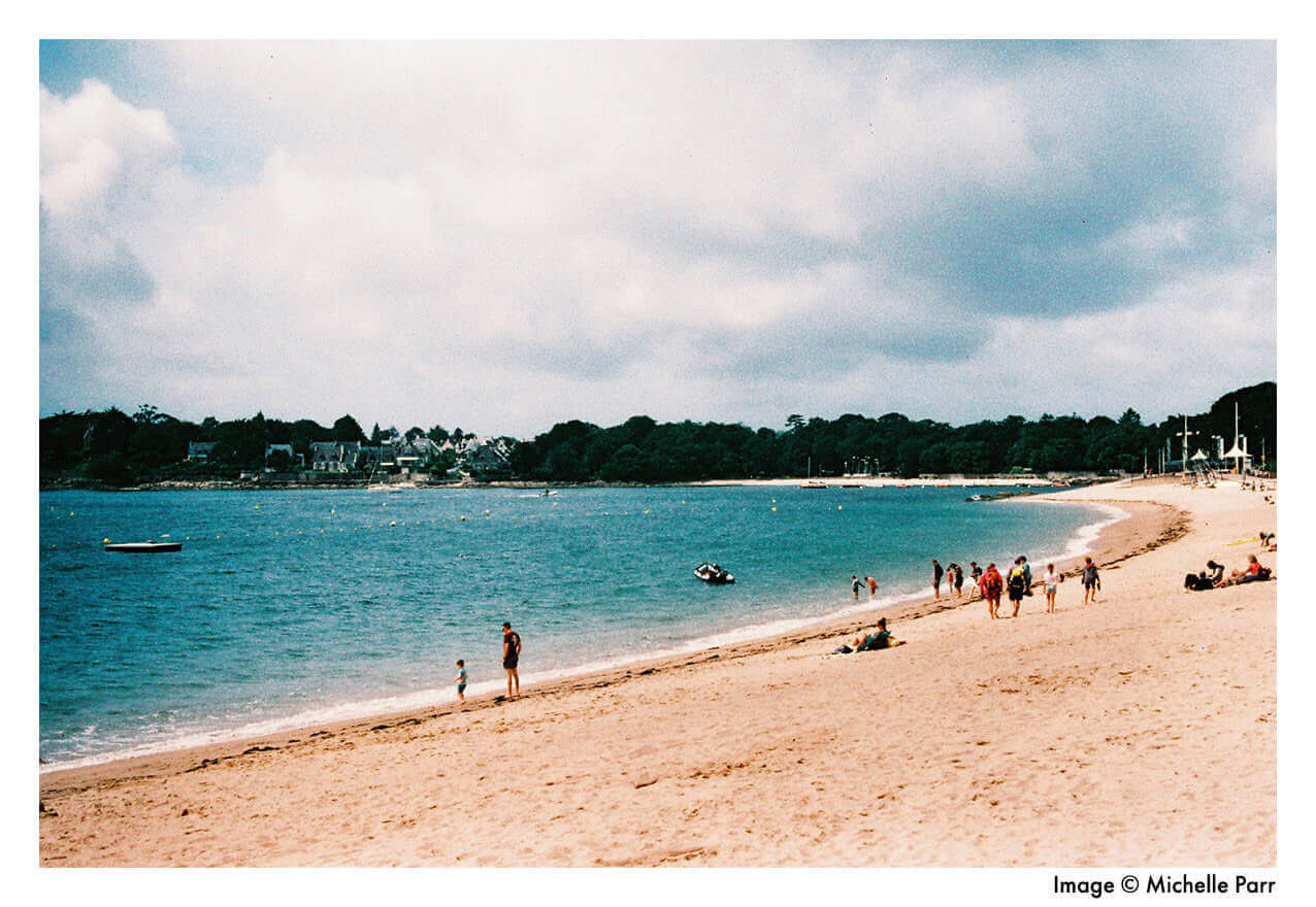 A scenic beach view with people enjoying the water and sand under cloudy skies.
