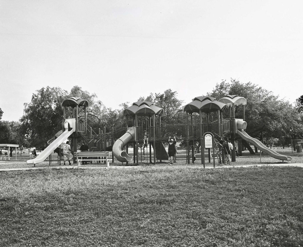 Black and white photo of a playground with slides and children playing in a park.