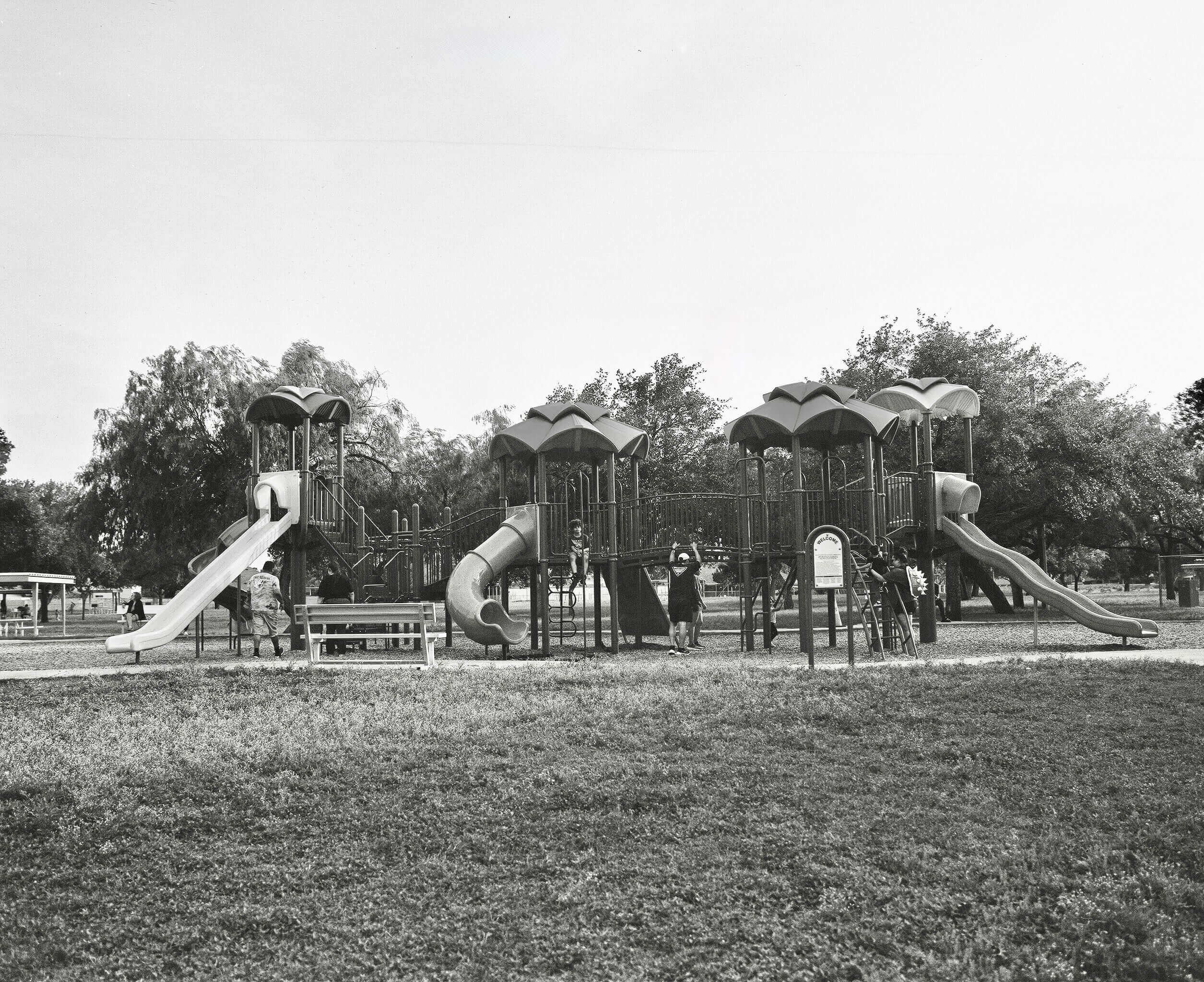 Black and white photo of a playground with slides and children playing in a park.