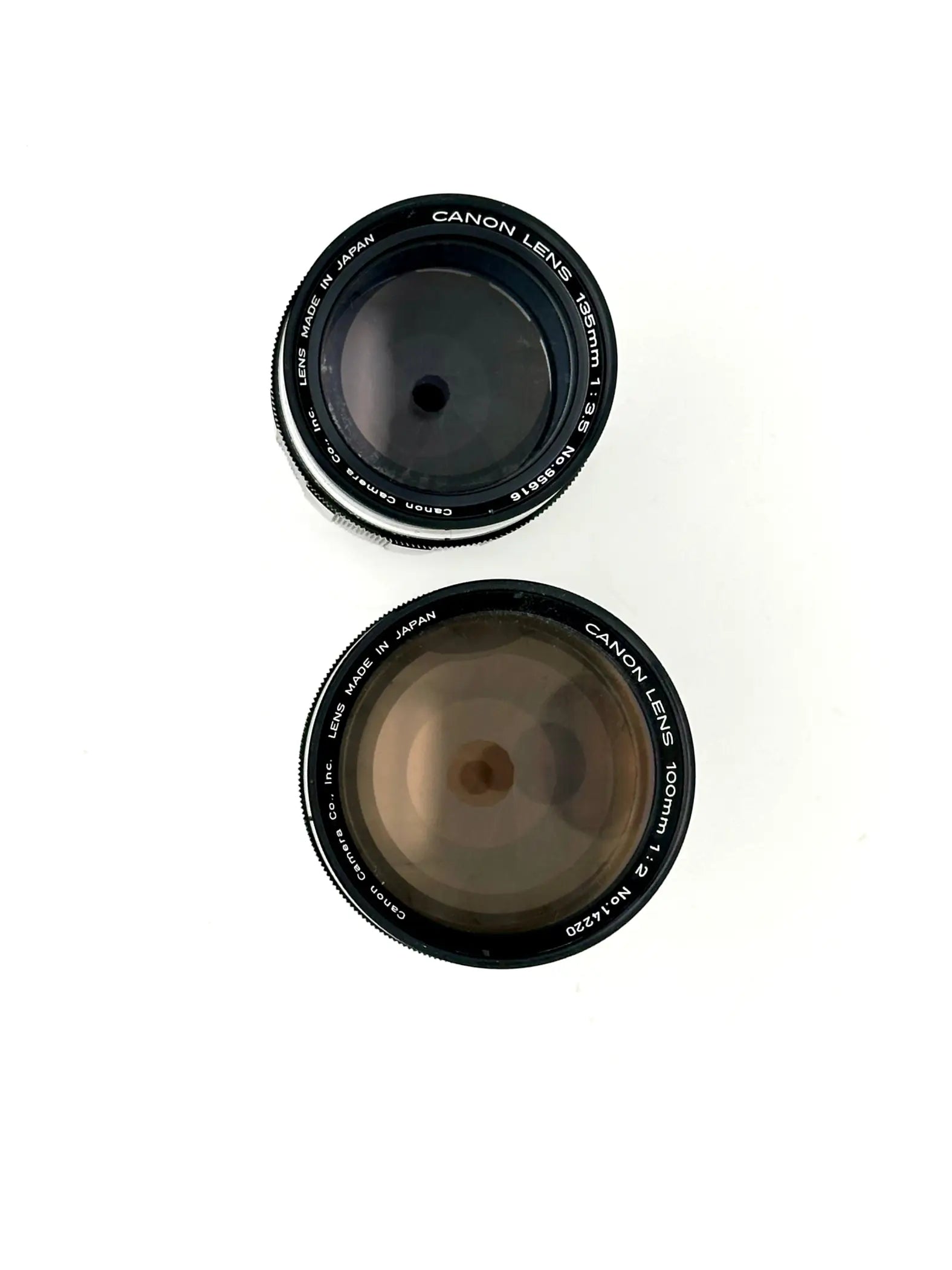 Two black canon camera lenses, one 50mm f/1.4 and the other 100mm f/2, with silver lettering on their rings.