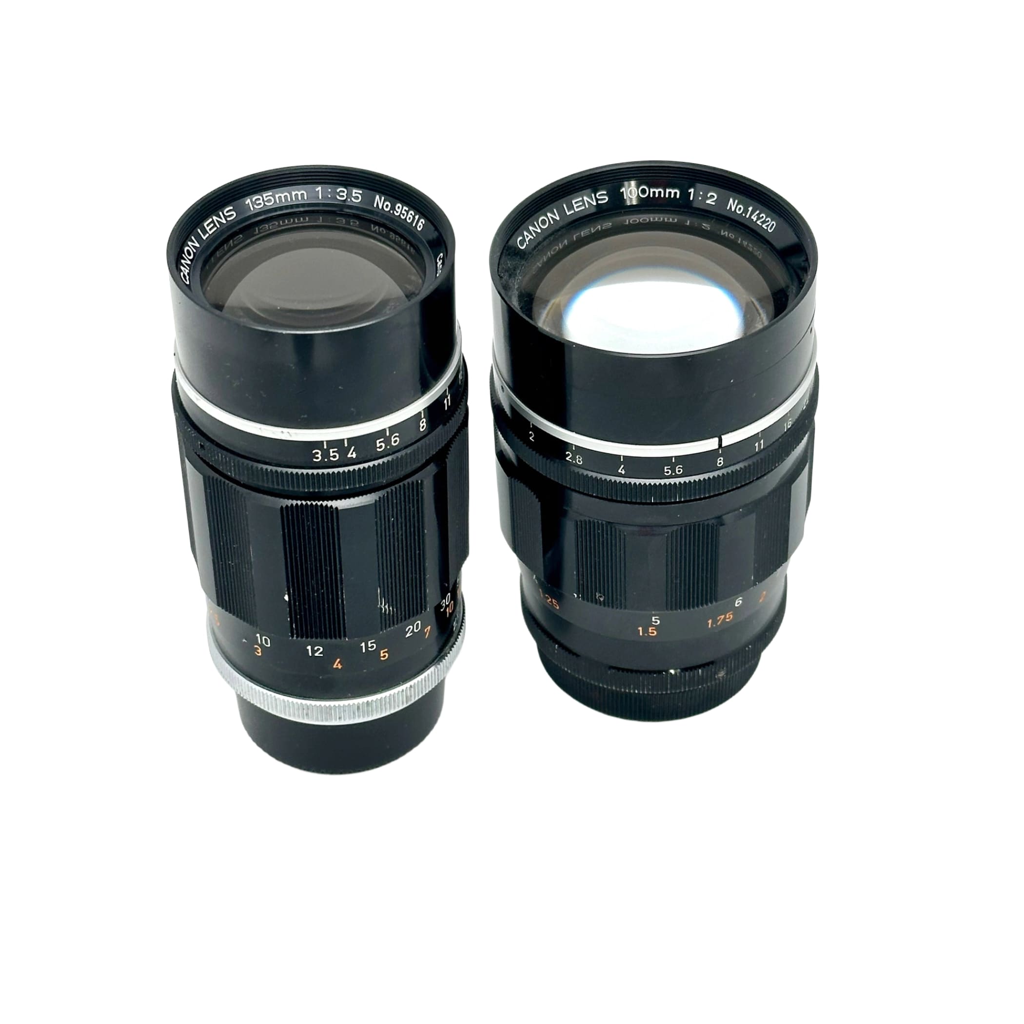 Two black canon camera lenses with silver metallic rings and engraved markings, one labeled 195mm f/3.5 and the other 100mm f/2.