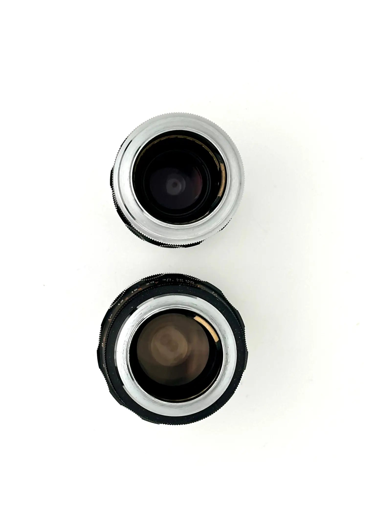 Two vintage camera lenses, one with a silver metallic rim and the other in black rubberized housing.