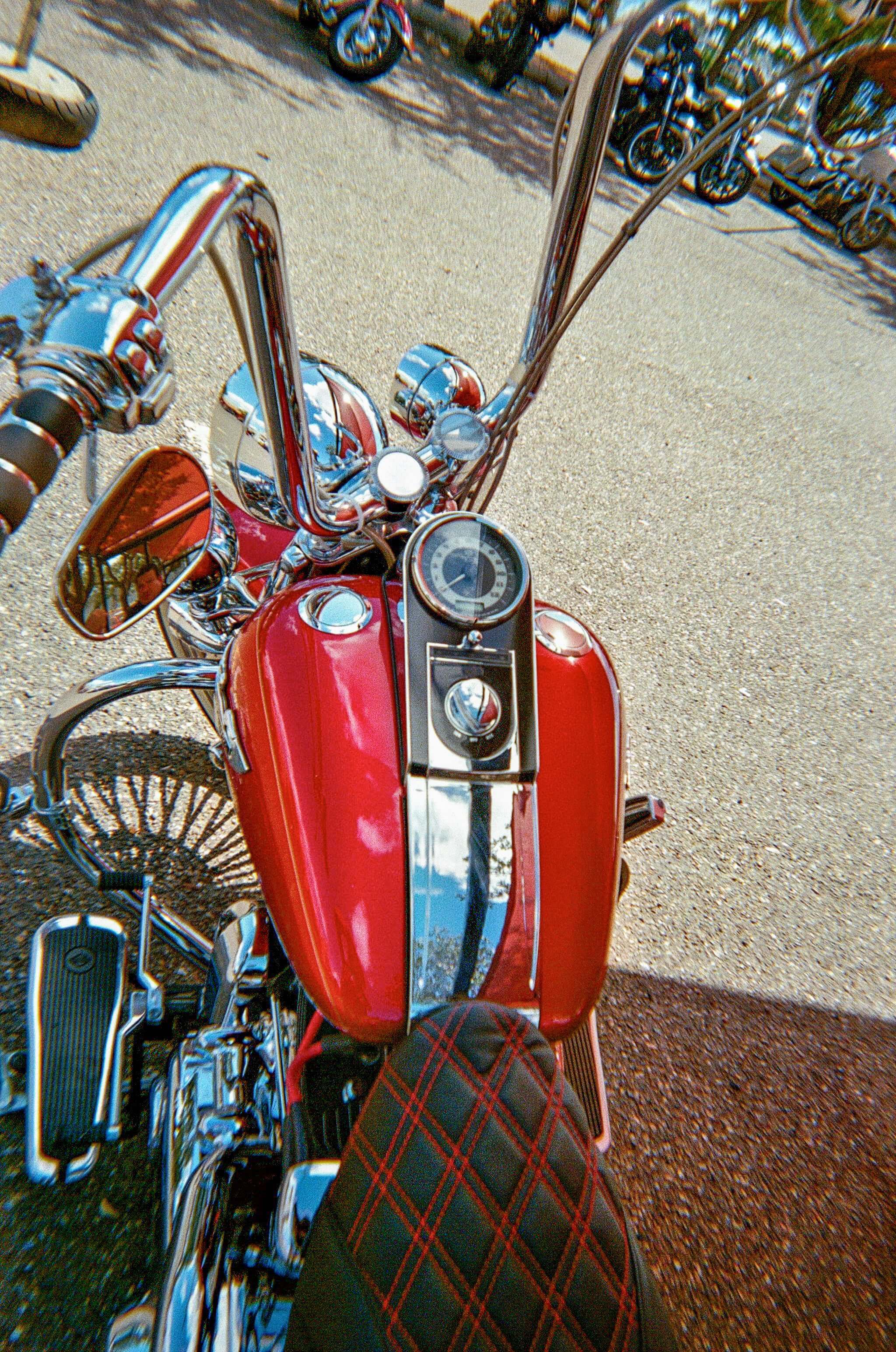 Close-up view of a vintage motorcycle with a red tank and chrome accents, showcasing the handlebars and speedometer.
