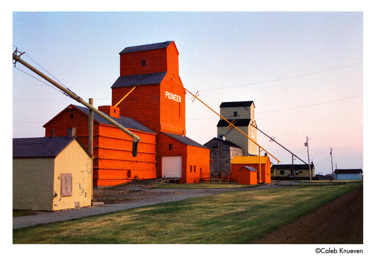 Colorful grain elevators at sunset in rural landscape with vibrant orange buildings.