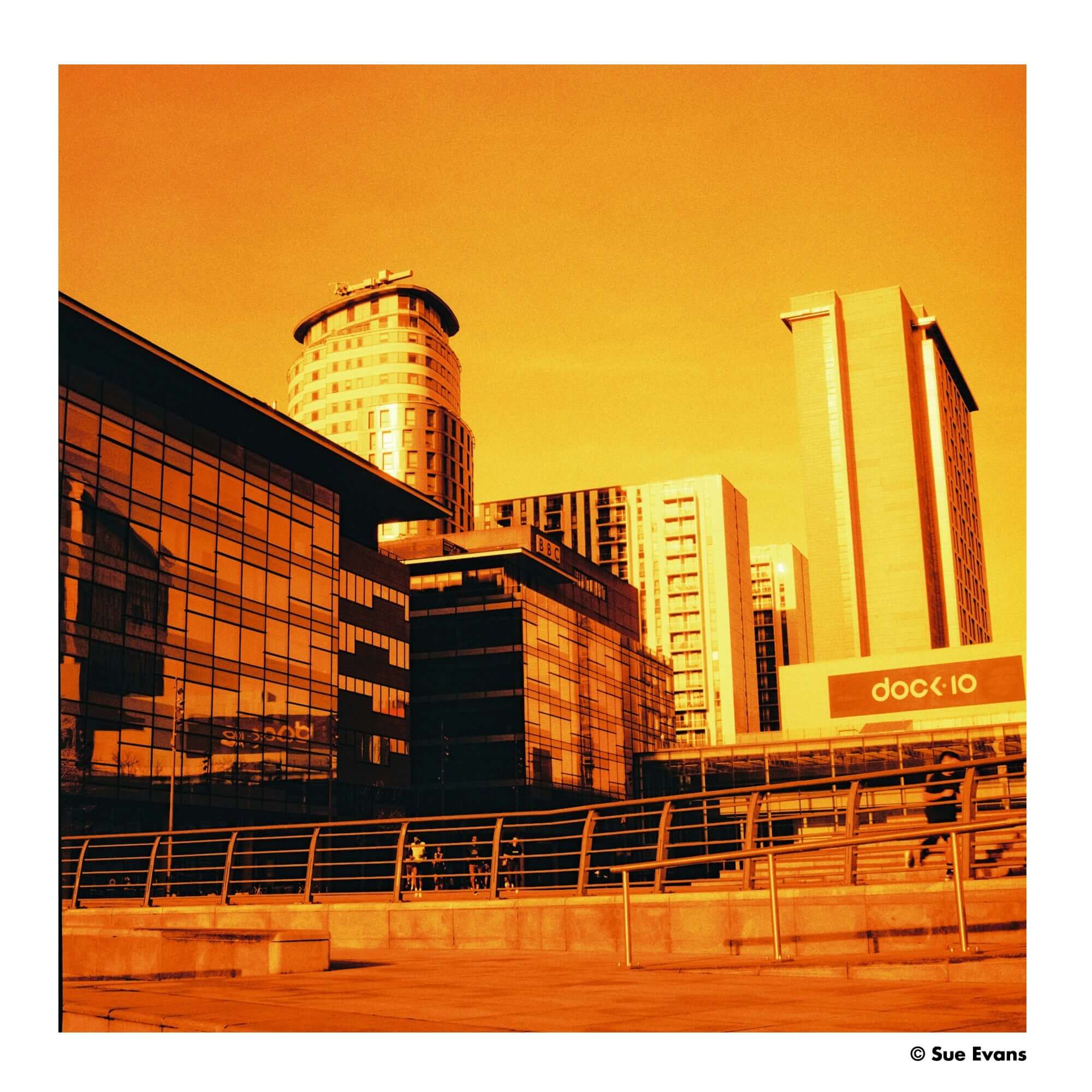 Modern glass-and-steel office buildings under a warm orange sky.