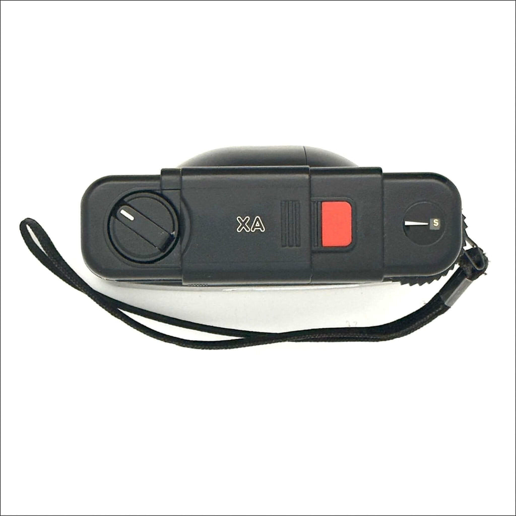 Black compact camera with red shutter button and ’xa’ branding on the top panel.