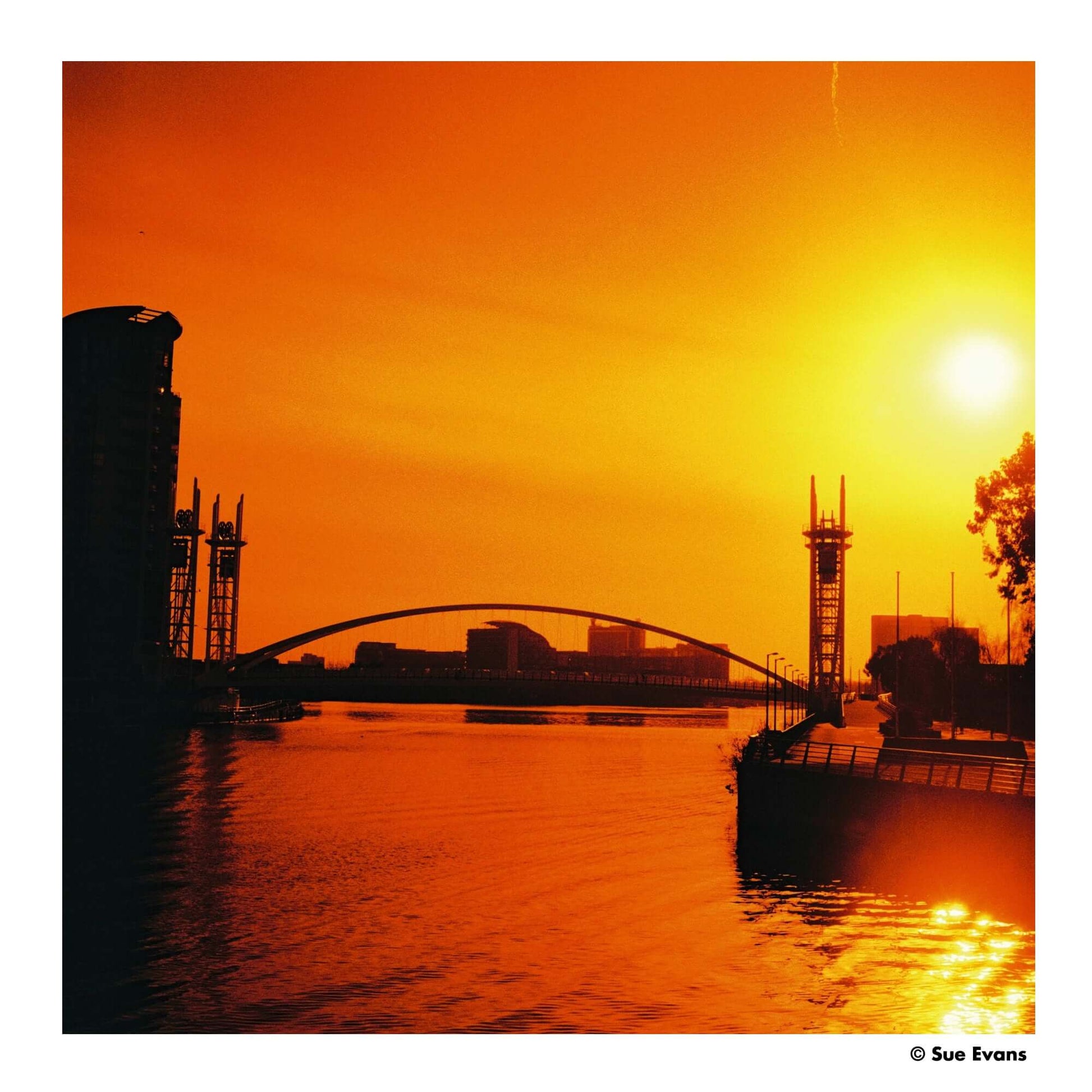Stunning sunset over a city river featuring vibrant orange hues and silhouettes of buildings and bridges.