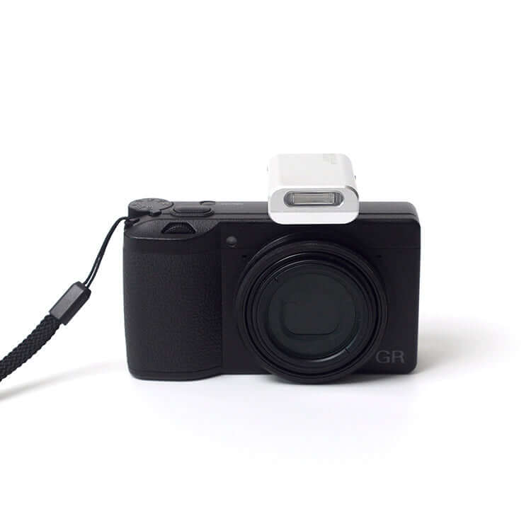 Black compact camera with a white flash attachment and black wrist strap.