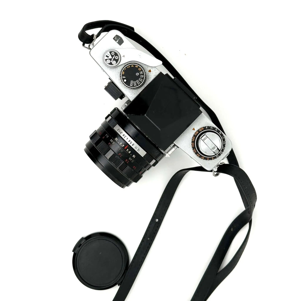 Silver-bodied film camera with a black lens and matching strap, featuring classic dials and controls.